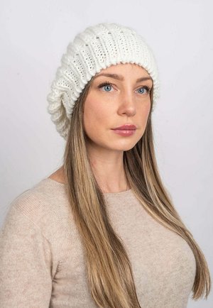 Beanie bianco lavorato a maglia con design a costine, caratterizzato da una vestibilità ampia e un orlo piegato. Texture morbida, su uno sfondo neutro.