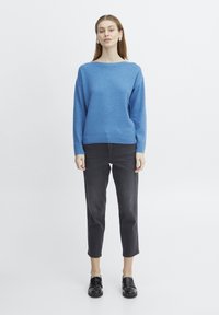 Pull en tricot bleu avec un large col, des manches longues et des poignets côtelés, assorti à un jean droit noir et des mocassins noirs brillants.
