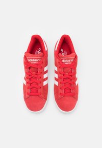 Κόκκινα σουέτ sneakers Adidas Campus με λευκές ρίγες, σχέδιο με κορδόνια, μαξιλαρωμένος γιακάς και λογότυπο στη γλώσσα. Στρογγυλή μύτη και καουτσούκ σόλα.