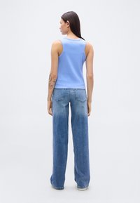 Ανοιχτό μπλε αμάνικο μπλουζάκι με απλό σχέδιο, σε συνδυασμό με ανοιχτό μπλε τζιν παντελόνι φαρδιάς γραμμής, με ξεβάμμένη υφή denim και κλασικό στιλ με πέντε τσέπες.