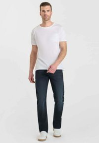 T-shirt blanc à manches courtes avec une poche texturée, associé à un jean bleu foncé et des baskets blanches avec des semelles marron clair.
