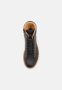 Botín de cuero negro hasta el tobillo con punta redonda, forro interior beige y suela de goma marrón. Presenta un diseño de cordones y detalles de costura mínimos.