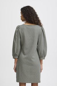 Un vestito a maniche corte con un tessuto verde texture, caratterizzato da un motivo geometrico a diamante color marrone chiaro, e una vestibilità rilassata con maniche a sbuffo.