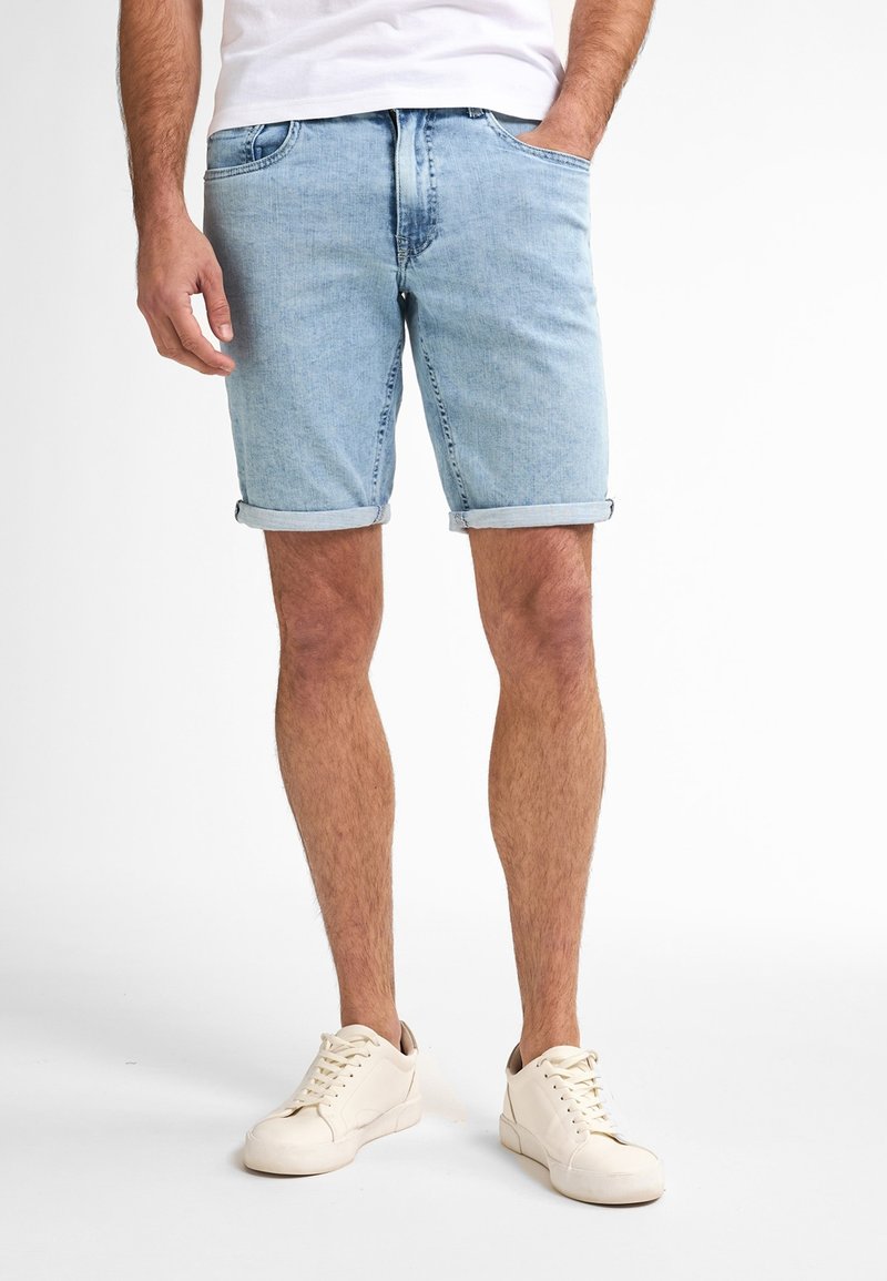 Shorts di jeans azzurri con risvolti, dotati di tasche frontali e design aderente. Indossati con sneaker beige e una maglietta bianca.