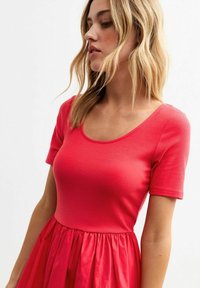 Red ribbed top with a scoop neckline and short sleeves, paired with a flowing, pleated skirt in a contrasting shade of red.