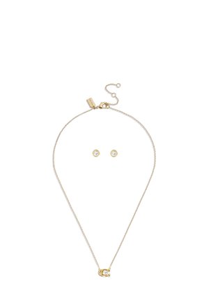 Kultainen kaulaketju hevosenkengän muotoisella riipuksella, jossa kirkas kristalli, yhdistettynä vastaaviin kultaisiin nappikorvakoruihin, joissa kirkkaat kristallit.