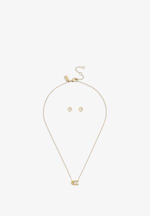 Collana in oro con ciondolo a forma di ferro di cavallo con cristallo trasparente, abbinata a orecchini a perno in oro con cristalli trasparenti.