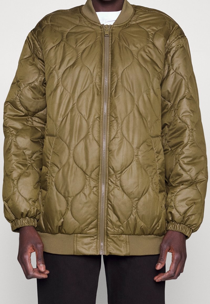 Kurtka bomberska w oliwkowej zieleni, pikowana, z przednim zamkiem błyskawicznym, ściągaczami na mankietach i dole, o gładkim, błyszczącym wykończeniu i wypełnionej teksturze.