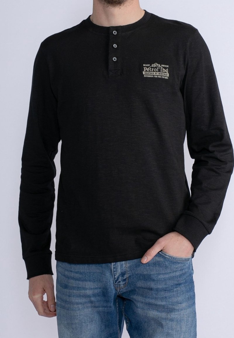 Mustapaita pitkällä hihalla, jossa on pyöreä kaula-aukko, kolmesta napista koostuva nappilista ja edessä beige logo. Pehmeä rakenne, istuva muotoilu ja rento tyyli.