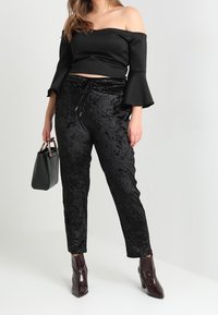 Svart av-axeln topp med trumpetärmar, matchad med svarta sammetbyxor med dragsko i midjan. Fulländad med glansiga ankelboots och en handväska.