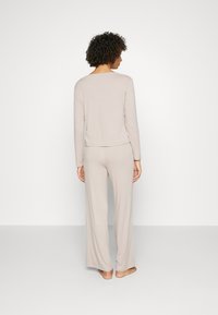 Helle beige Lounge-Wear-Kombination mit einem langärmeligen Oberteil und weiten Hosen, die eine weiche Textur und einen lässigen Schnitt aufweisen.