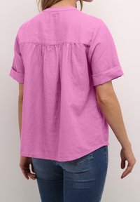 Rosa, kortärmad, knäppt skjorta i lätt tyg med en rynkad rygg och uppvikta ärmar. Stylad med denimjeans.