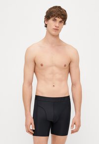 Μαύρα μποξεράκια με λείο υφή και ελαστική μέση που διαθέτει το όνομα της μάρκας. Η εφαρμογή είναι στενή με σχεδιασμό που αγκαλιάζει.