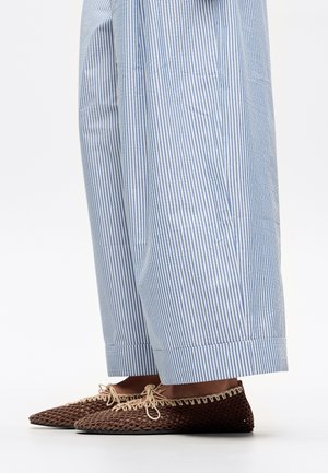 Scarpe slip-on intrecciate marroni con design a punta, abbinate a pantaloni a righe blu chiaro e bianchi, caratterizzati da una vestibilità ampia e orli risvoltati.