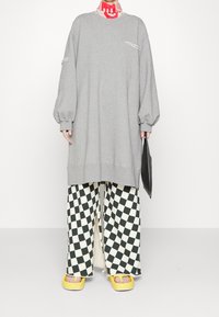 Överdimensionerad grå sweatshirt med sänkta axlar och ficka; kombinerad med svartvit rutig vida byxor; gula plattformssandaler.