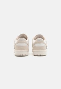 Ténis Nike em camurça bege claro com acabamentos em tecido texturizado e sola de borracha. Apresenta um logótipo em relevo no calcanhar.