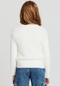 Maglione bianco con una texture morbida sul retro e maniche lunghe a costine. L'orlo inferiore è in maglia bianca solida, abbinato a pantaloni corti in denim blu.