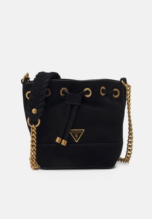Black bucket bag with gold chain strap, braided leather detail, drawstring closure, and gold GUESS logo on front.