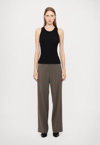 Top sans maniche nero realizzato in materiale elasticizzato, abbinato a pantaloni marroni a vita alta e a gamba larga. Texture liscia, design minimale.