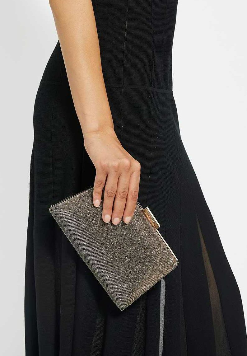 Metallic clutch purse with a textured surface, featuring a clasp closure. The color is a shiny silver-gold, held in a hand against a black dress.