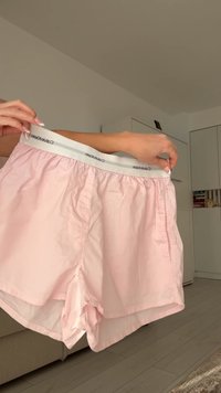 Light pink shorts with a white elastic waistband featuring a gray stripe. The fabric appears smooth and lightweight, with side pockets.