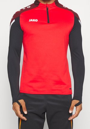 Mann trägt ein rotes und schwarzes langärmeliges Sportoberteil mit Daumenlöchern und schwarze Sporthose mit orangefarbenen Streifen.