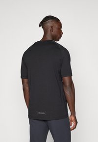Camiseta negra de manga corta con cuello redondo, que presenta una textura suave y un sutil detalle del logo en el dobladillo trasero.