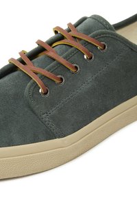 Sneaker grigio in suede con lacci in pelle marrone e occhielli metallici, dotata di una suola in gomma beige texturizzata.