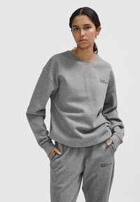 Grau Sweatshirt mit Rundhalsausschnitt und langen Ärmeln, versehen mit einem Frontdruck mit der Aufschrift "HALO 19681973." Das Material scheint weich und strukturiert zu sein.