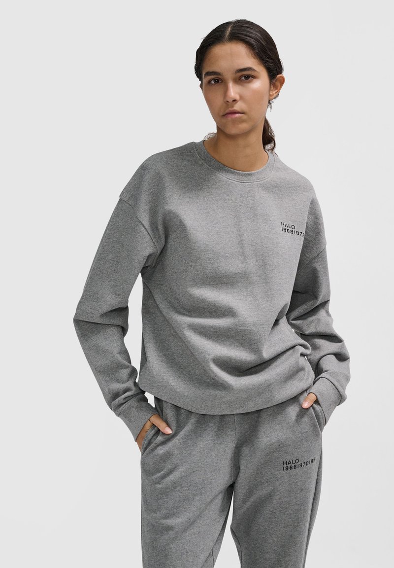 Grau Sweatshirt mit Rundhalsausschnitt und langen Ärmeln, versehen mit einem Frontdruck mit der Aufschrift "HALO 19681973." Das Material scheint weich und strukturiert zu sein.