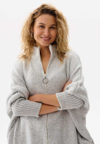 Jasnoszary sweter z dzianiny z zamkiem błyskawicznym przy kołnierzu i oversize'owymi rękawami. Posiada ribbowe mankiety i boczne kieszenie. Miękka tekstura i luźny krój.