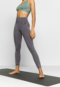 Legginsy w kolorze fioletowym z wysokim stanem, o teksturowanym wykończeniu, zestawione z sportowym biustonoszem w kolorze szałwii. Oba elementy charakteryzują się minimalnym logo i bezszwowym designem.