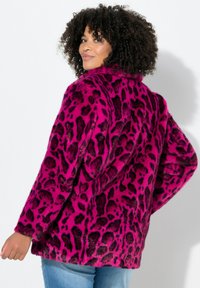 Chaqueta de piel sintética en rosa brillante con estampado de leopardo negro. Presenta un cuello alto y un corte relajado, combinada con unos vaqueros de denim azul claro.