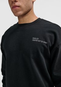 Svart sweatshirt i bomull med rund halsringning och åtsittande muddar. Broderad text "HALO 196819721981" på bröstet.