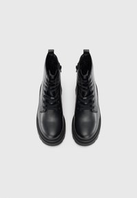 Bottines en cuir noir avec une finition texturée, à lacets sur l'avant et fermeture éclair sur le côté. Semelle en caoutchouc épaisse pour plus de stabilité.