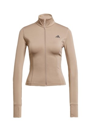 Giacca sportiva beige con collo alto, chiusura con zip integrale e maniche lunghe. Presenta il logo Adidas sulla parte superiore sinistra. Texture liscia.