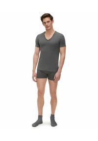 T-shirt grigia a V con maniche corte abbinata a pantaloni boxers coordinati e calzini alla caviglia, caratterizzata da una morbida texture e un design minimalista.