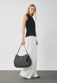 Sac en cuir noir texturé avec une forme courbée, des détails en or et un accent à frange. Porté avec une bandoulière, présentant un subtil motif géométrique.