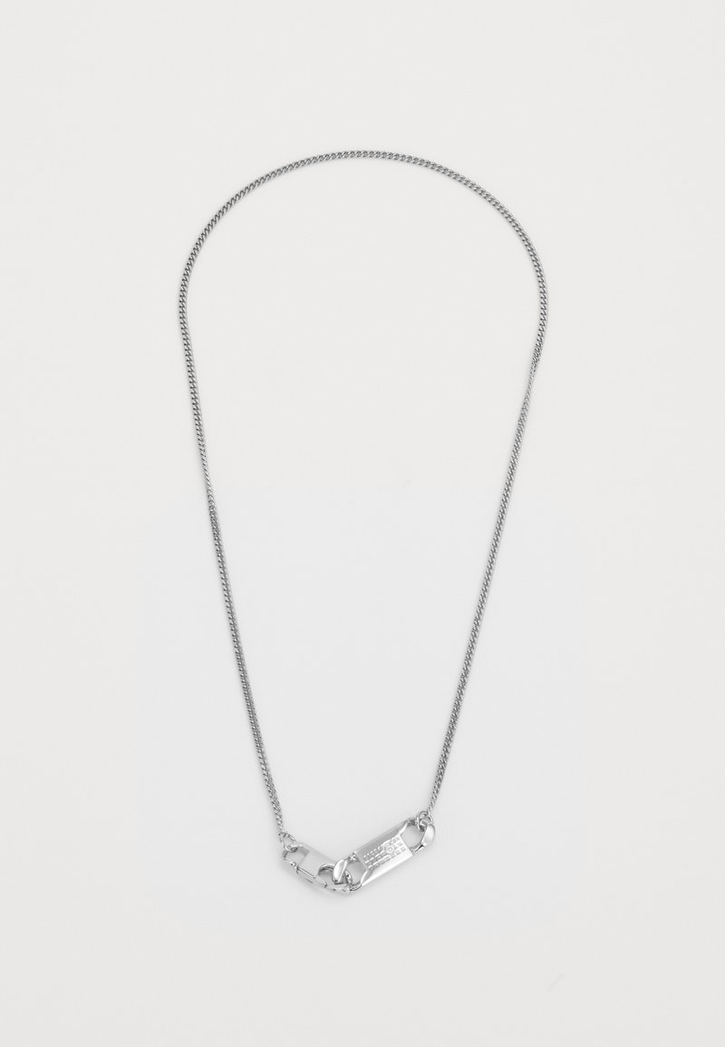 Collana d'argento con una catena sottile e attorcigliata e una chiusura centrale rettangolare con testo inciso. Texture liscia, design minimalista.