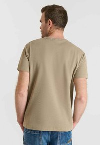 Camiseta de algodón color beige de manga corta con una superficie texturizada, cuello redondo y un corte holgado, vista desde la parte trasera.