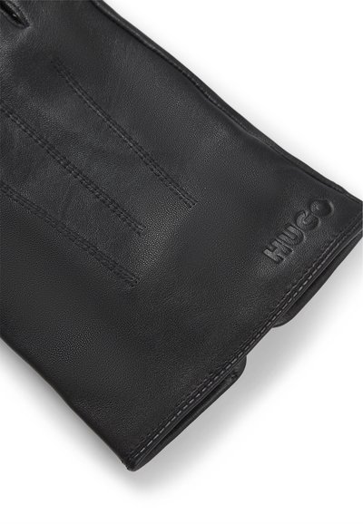 Gant en cuir noir avec une texture lisse, comportant trois lignes cousues au dos et un logo "HUGO" en relief au niveau du poignet.