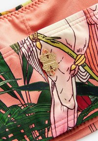 Mehrfarbiges Gewebe mit einem tropischen Druck in Grüntönen und Rosa, akzentuiert durch einen goldenen dekorativen Verschluss mit filigranen Details.