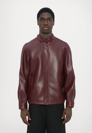 Burgundy faux læderjakke med høj krave, raglanærmer, to sidelommer og kontrastsyede detaljer. Glat tekstur.