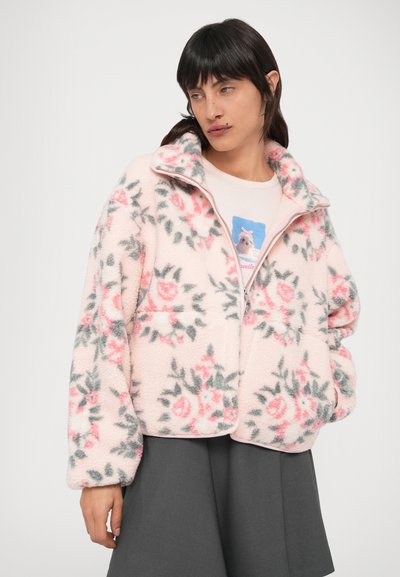 Fleecová bunda v pastelovo ružovej farbe s kvetinovým vzorom v ružovej a sivej. Má vysoký golier, zapínanie na zips a predné vrecká.