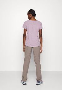 Lichtpaarse korte mouw top met een geplooide achterkant, gecombineerd met beige broek en grijs-paarse sneakers, op een model gezien vanuit de achterkant.