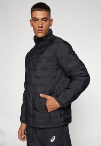 Black padded jacket with a high collar, featuring horizontal stitching and zippered pockets. Smooth texture, lightweight design, and secure fit.
