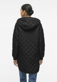 Črna prešita jakna s kapuco, dolga in sproščena, z ribastimi manšetami. Tekstura je gladka, z detajlom v obliki diamanta.