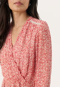 Vestido floral en crema claro con patrones rojos y rosas, que presenta un escote en V profundo y una textura fruncida en los hombros y la cintura.