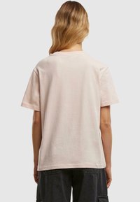 Camiseta de algodón de color rosa claro con un corte relajado, mangas cortas y cuello redondo. Textura suave y diseño simple sin marcas visibles.