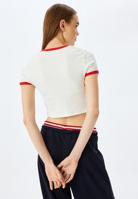Hvid ribbet crop top med rød kant ved ærmer og halslinning, parret med marineblå bukser med en rød og hvid stribet talje.